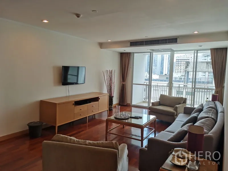 公寓 出租在Khlong Toei, Bangkok - 朝向城市的客厅，成套沙发、壁挂电视，大推拉门连接明亮阳台。