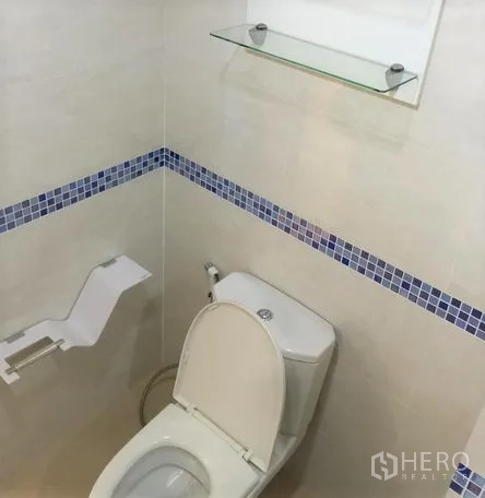 Condominium for rent in Watthana, Bangkok - Toilet corner with blue mosaic border, handheld bidet spray and glass shelf.