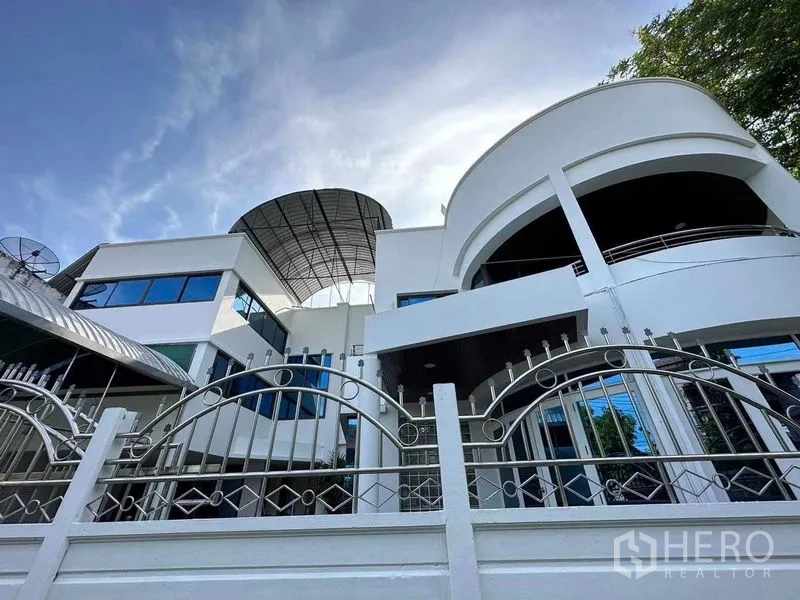 Home Office for sale - Low-angle view of gated modern home office with curved balconies and metal fence.
