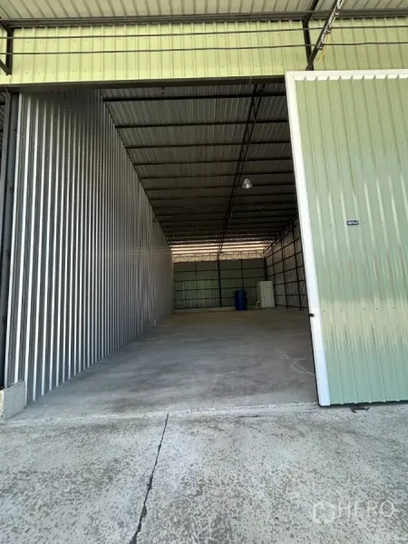 Warehouse for rent in Ban Pho, Chachoengsao - Tall sliding warehouse door opening to a drive-in bay with corrugated metal walls and concrete floor.
