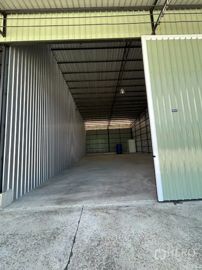 Warehouse for rent in Ban Pho, Chachoengsao - Tall sliding warehouse door opening to a drive-in bay with corrugated metal walls and concrete floor.