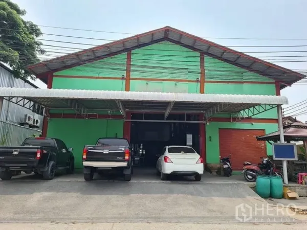 Warehouse for sale in Mueang Samut Prakan, Samut Prakan - Front facade of a green gable-roof warehouse with a wide roller shutter and covered loading bay in Mueang Samut Prakan.