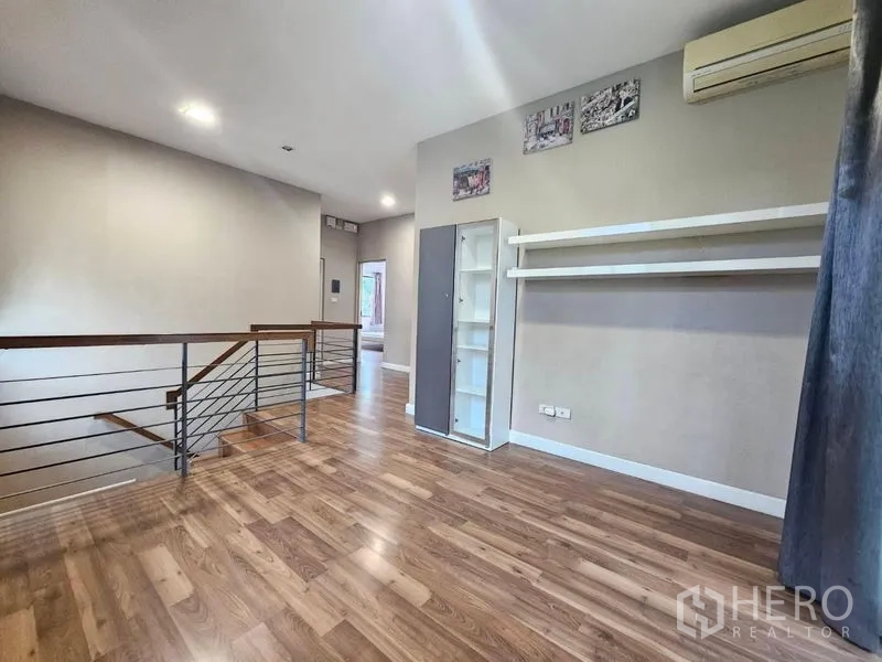 Detached House for sale in Prawet, Bangkok - Upstairs landing with metal railing, wood floors, display shelves and air conditioner.