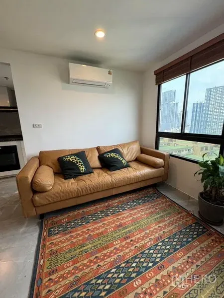 公寓 出租或出售 - 明亮客厅，棕色真皮沙发、花纹地毯、空调与大窗城市景观。