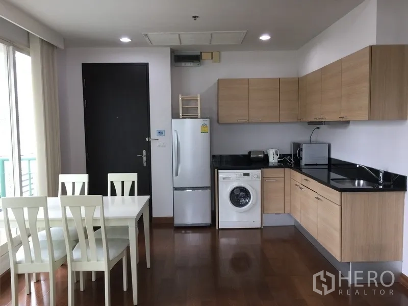 Condominium for rent in Pathum Wan, Bangkok - Open kitchen with wood cabinets, black countertops, fridge, washing machine and dining table.