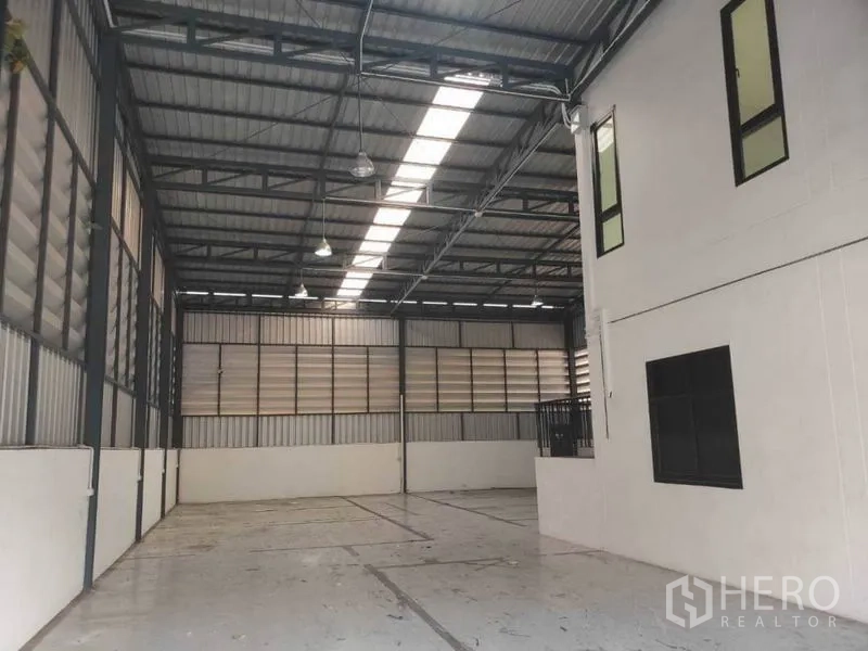 Warehouse for rent in Lam Luk Ka, Pathum Thani - Spacious high-ceiling warehouse interior with steel trusses and skylight panels.
