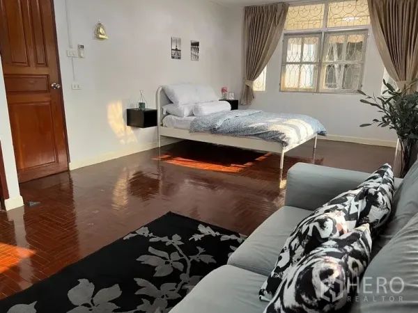Home Office for rent in Suan Luang, Bangkok - Spacious bedroom with parquet flooring, bed and sofa, and large curtained windows.