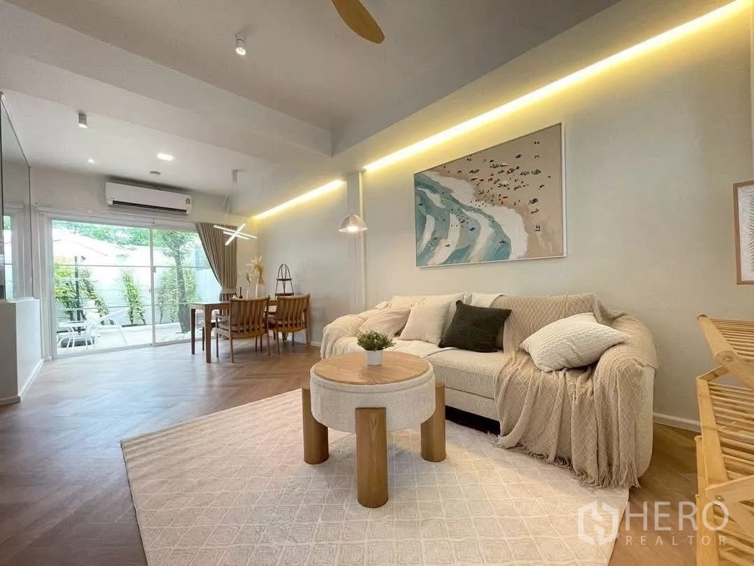 联排别墅 出租在Prawet, Bangkok - 舒适客厅与餐区，沙发、装饰画，落地推拉门通往露台。