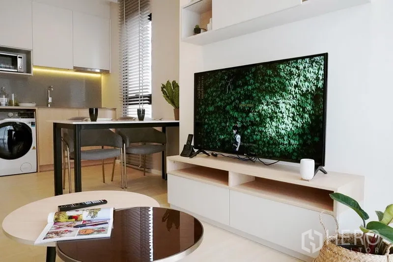 公寓 出租在Pathum Wan, Bangkok - 电视墙与圆形茶几，后方是简洁厨房与用餐区