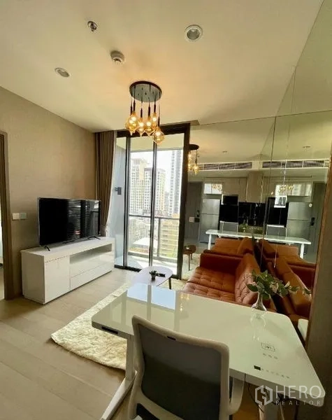 公寓 出租在Ratchathewi, Bangkok - 明亮客厅，橙色皮沙发、镜面墙、电视柜与城市景观阳台。