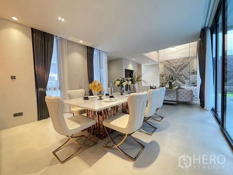 Detached House for sale in Suan Luang, Bangkok - Elegant dining area with a marble table, six white chairs and full-height windows beside the living space.