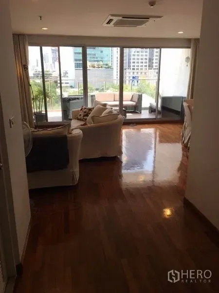 Condominium for rent in Pathum Wan, Bangkok - Open-plan living area with polished wood floors and floor-to-ceiling glass doors leading to a balcony with city views.
