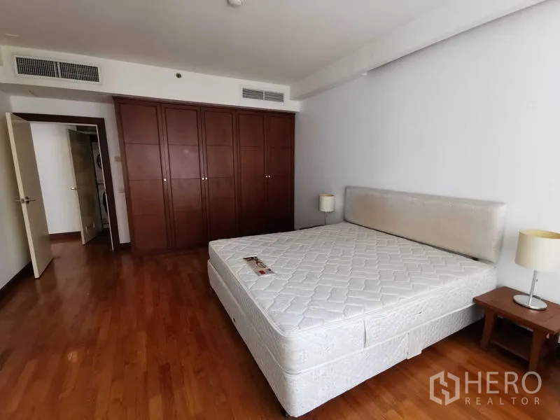 Condominium for rent in Pathum Wan, Bangkok - Spacious bedroom with large built-in wardrobe, wood floors, and bedside tables.
