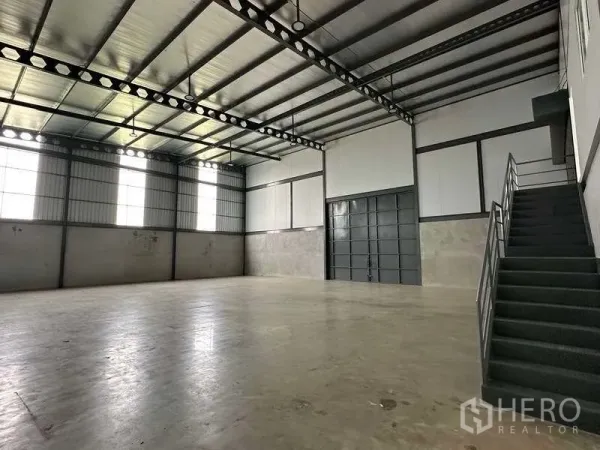 คลังสินค้า ให้เช่าในSamut Prakan - พื้นที่คลังสินค้าโล่ง เพดานโครงเหล็กสูง พื้นคอนกรีต หน้าต่างสูง และบันไดโลหะ