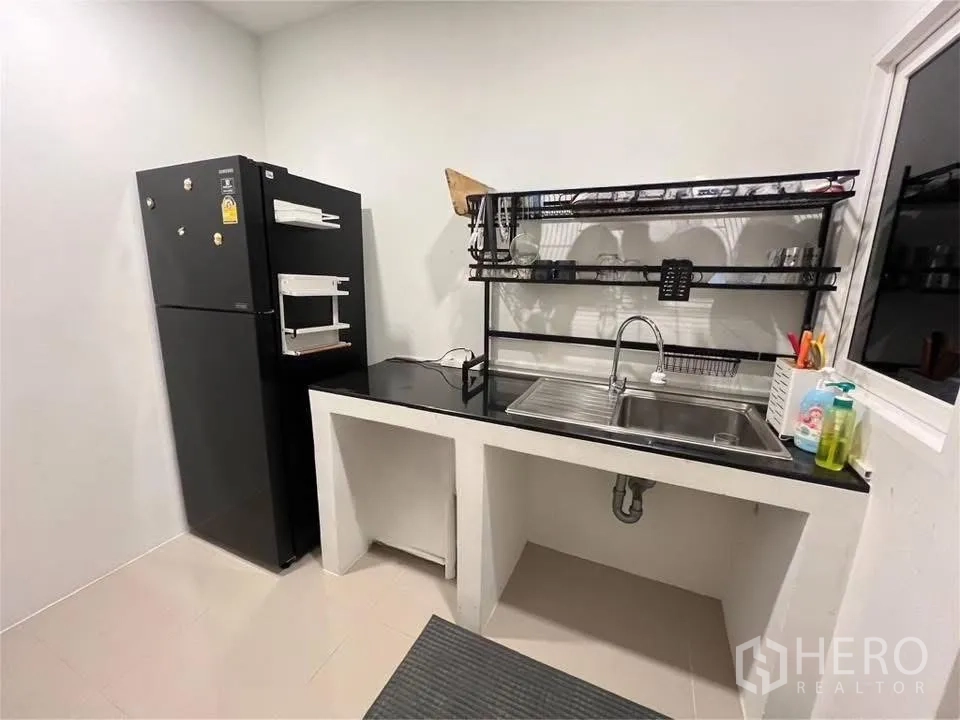 บ้านเดี่ยว for rent in Prawet, Bangkok - ครัวอีกส่วนมีตู้เย็น อ่างล้างจาน เคาน์เตอร์ดำ และชั้นคว่ำจานโลหะ.