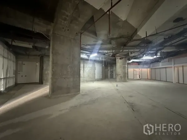 零售空间 出租 - 工业风室内，多个承重柱与粗糙墙面，天花安装管线及喷淋系统。