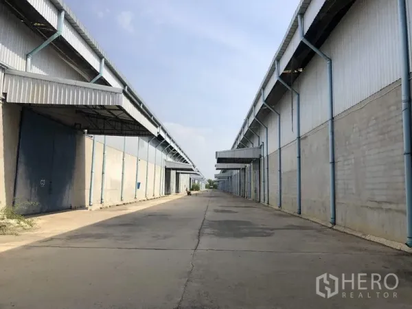 Warehouse for rent in Saraburi - Wide concrete access road between large industrial warehouse blocks with loading canopies in Saraburi.