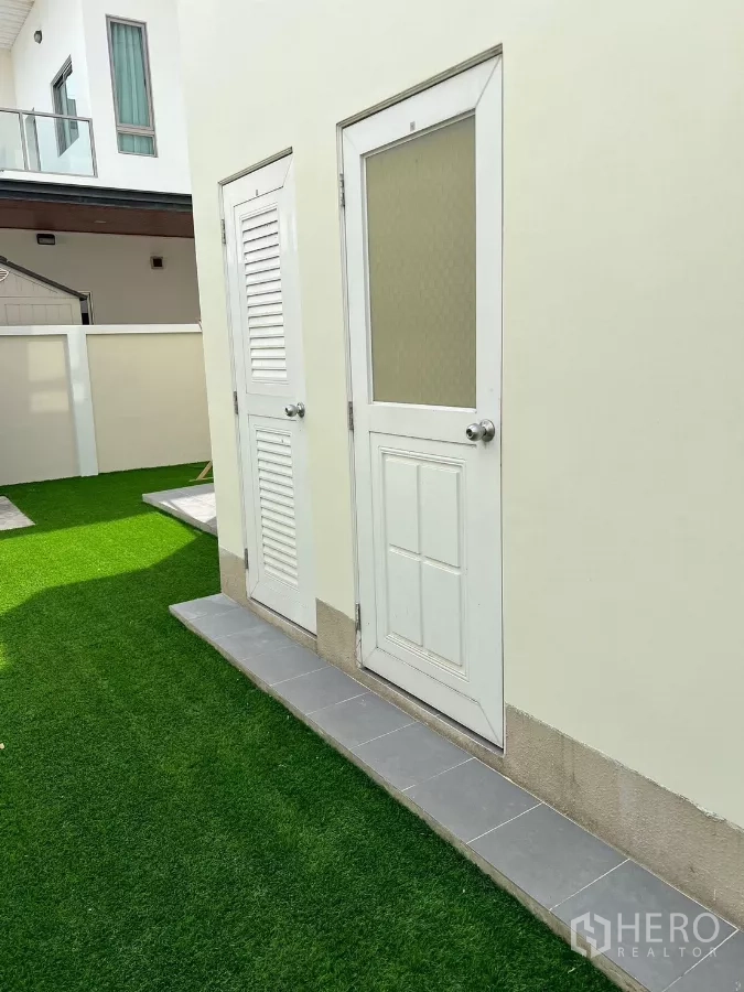 独立式住宅 出租在Bang Phli, Samut Prakan - 侧院服务区，白色门与人工草坪