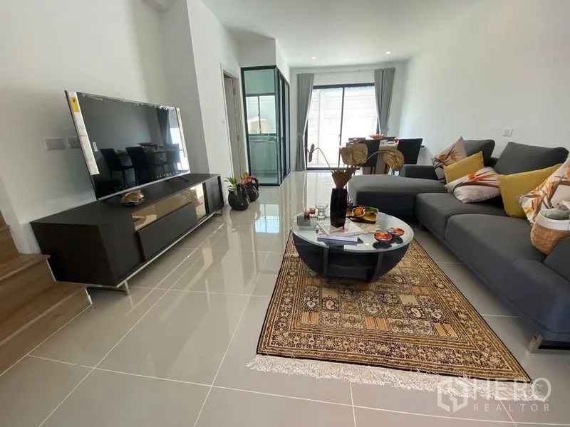 Townhouse for rent in Bang Kapi, Bangkok - Open-plan living and dining area with sectional sofa, TV console, and sliding glass doors.