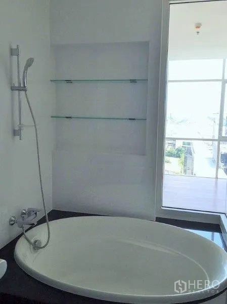 公寓 出售在Bang Na, Bangkok - 窗边椭圆浴缸，带玻璃置物架与城市景观。