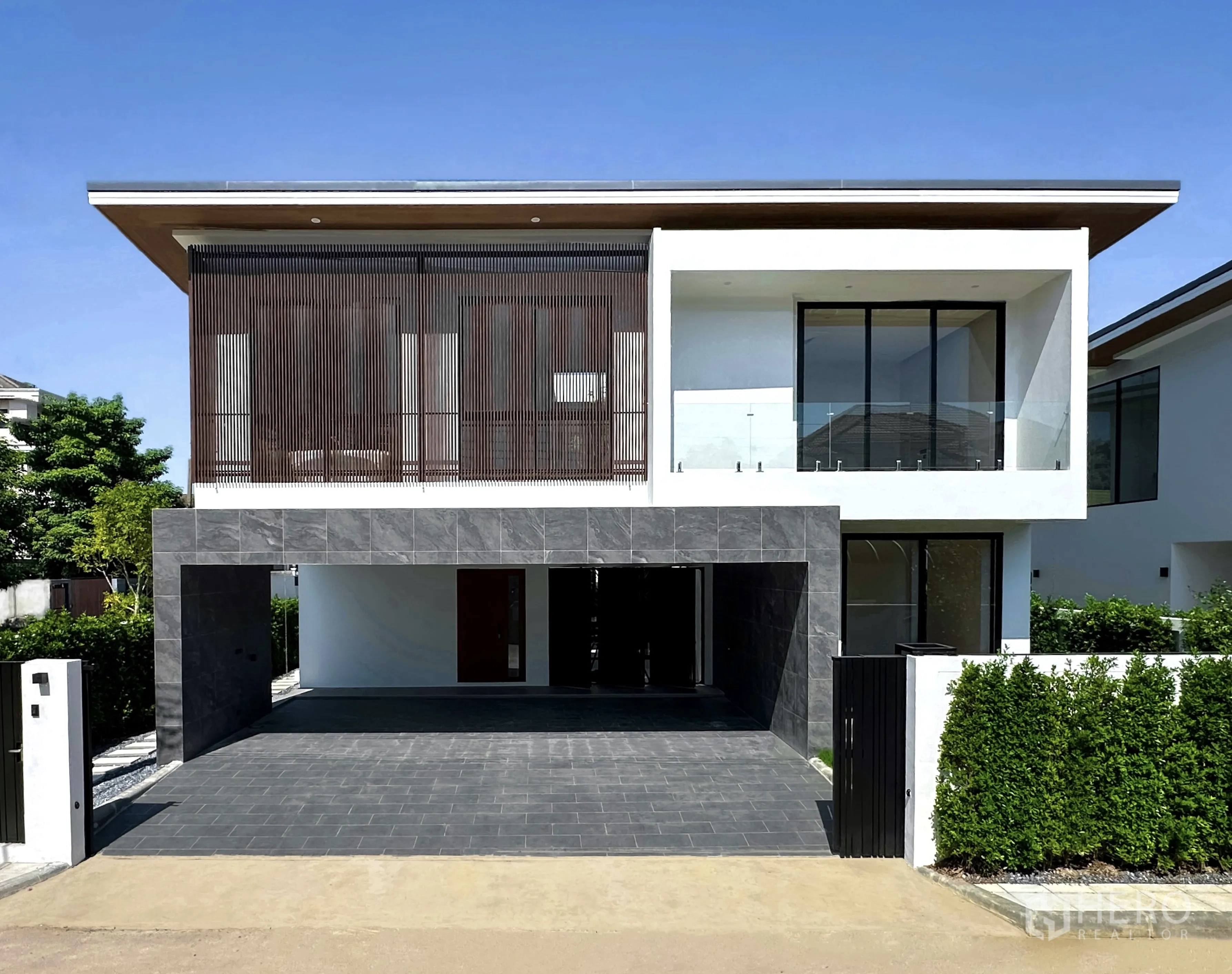 独栋房屋 for sale in Prawet, Bangkok - 两层现代热带风独栋别墅正面，设木质格栅、玻璃阳台、石材车库与大门车道。