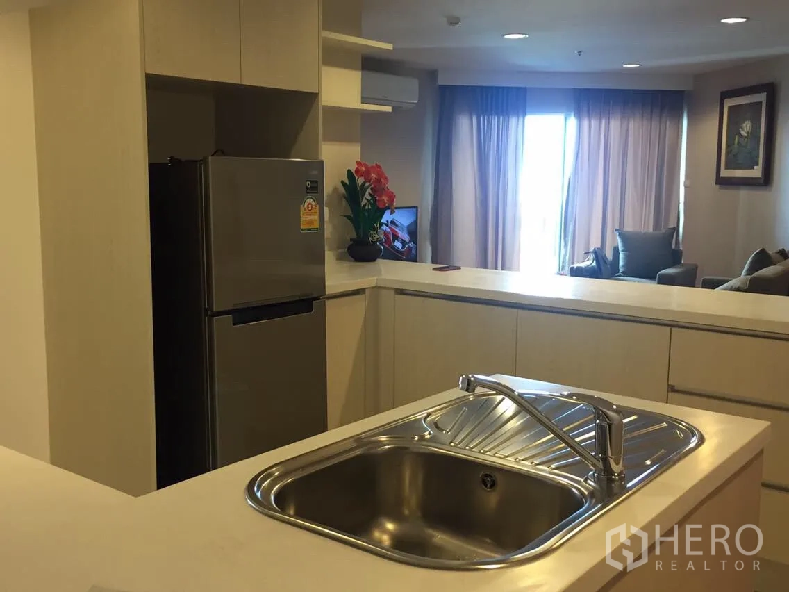 Condominium for rent in Huai Khwang, Bangkok - Open-plan kitchen with island sink, built-in cabinetry and stainless refrigerator facing a bright living area with balcony.