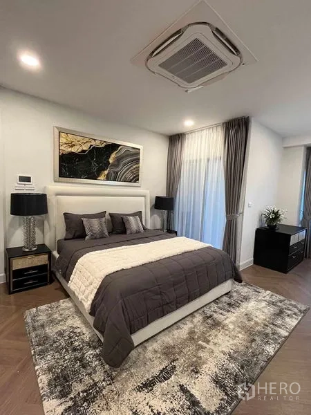 Detached House for rent in Saphan Sung, Bangkok - Master bedroom with upholstered headboard, ceiling cassette AC, grey bedding, artwork and full-height curtains.