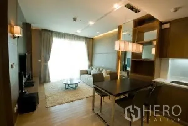 คอนโด ให้เช่าในKhlong Toei, Bangkok - มุมรับประทานอาหารพร้อมโคมไฟห้อย มองไปยังห้องนั่งเล่นและครัวขนาดกะทัดรัด มีผ้าม่านสูงจรดเพดาน