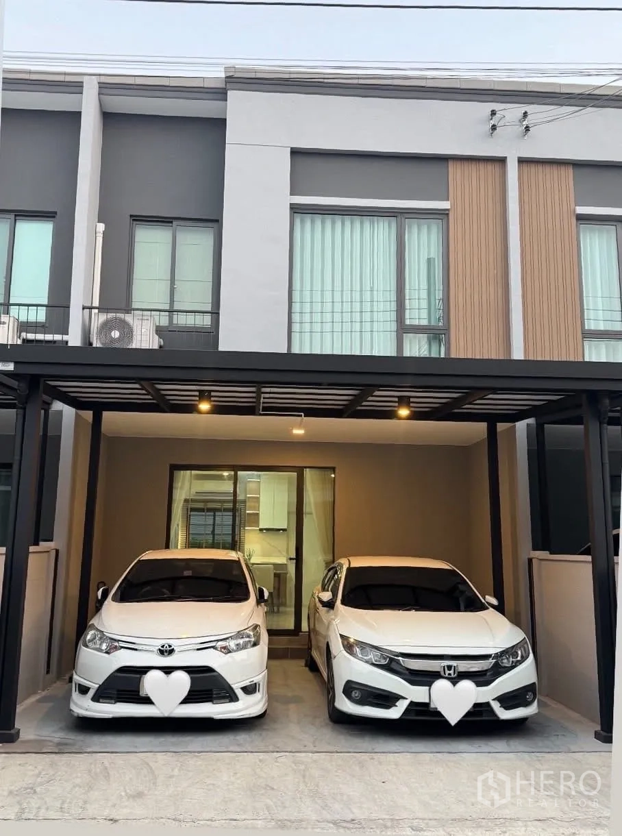 联排别墅 for rent in Bang Phli, Samut Prakan - 两层联排别墅正面，带可停两辆车的有顶车棚与推拉玻璃门。