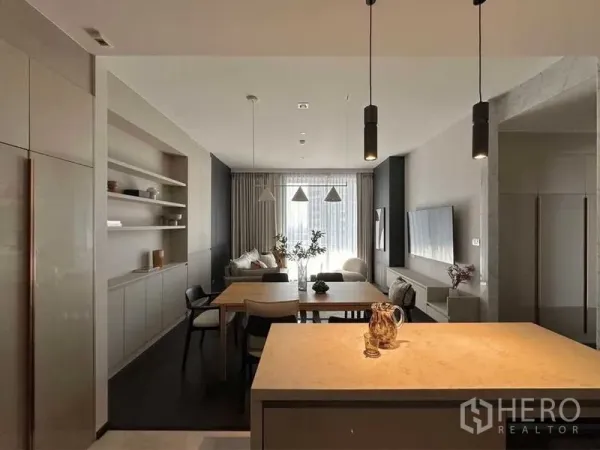 Condominium for rent or sale in Watthana, Bangkok - Wide view from kitchen island to dining and lounge with pendant lights and TV wall.