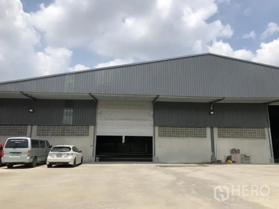 คลังสินค้า ให้เช่าในBang Kruai, Nonthaburi - มุมมองด้านหน้าโกดังสีเทาพร้อมประตูม้วนขนาดใหญ่และลานจอดกว้าง