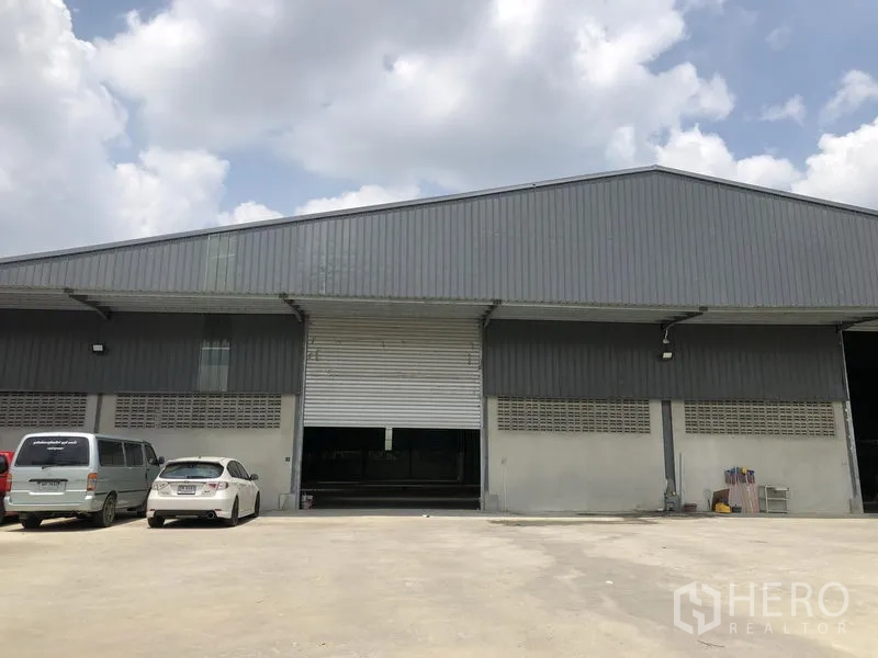 คลังสินค้า ให้เช่าในBang Kruai, Nonthaburi - มุมมองด้านหน้าโกดังสีเทาพร้อมประตูม้วนขนาดใหญ่และลานจอดกว้าง