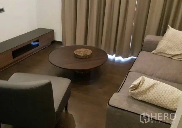 คอนโด ให้เช่าหรือขายในWatthana, Bangkok - มุมนั่งเล่นพื้นไม้เข้ม โต๊ะกลางทรงกลม ตู้วางทีวี และผ้าม่านสีเอิร์ธโทน