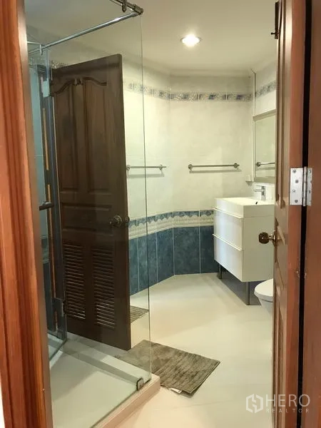 Condominium for rent in Watthana, Bangkok - Bathroom with glass-enclosed shower, white vanity and tiled walls.