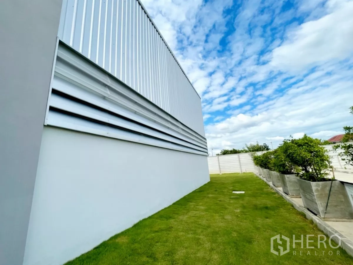 คลังสินค้า ขายในLam Luk Ka, Pathum Thani - ผนังโกดังติดช่องลม โดยมีแถบสนามหญ้าและกระถางต้นไม้เรียบร้อย