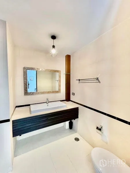 Townhouse for rent in Khlong Toei, Bangkok - White tiled bathroom featuring a large vanity with square basin and framed mirror.