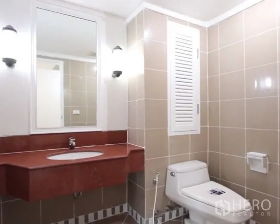 房间 出租在Khlong Toei, Bangkok - 米色浴室，红色石面洗手台、壁灯与坐便器。