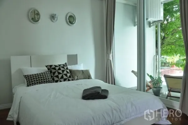 Townhouse for rent or sale in Watthana, Bangkok - Bedroom with floor-to-ceiling glass opening to a balcony with leafy views.