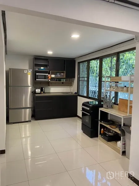 ทาวน์เฮาส์ ให้เช่าในKhlong Toei, Bangkok - ภาพมุมกว้างของครัว มีเตาอบ-เตาแก๊ส ชั้นวางของ หน้าต่างบานใหญ่ และพื้นกระเบื้องเงา