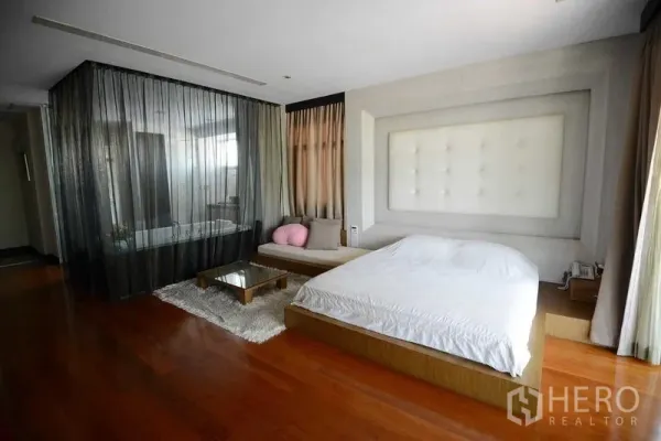 Detached House for sale in Bang Kapi, Bangkok - Spacious master bedroom with platform bed, sofa nook and a glass-enclosed bath behind sheer drapes