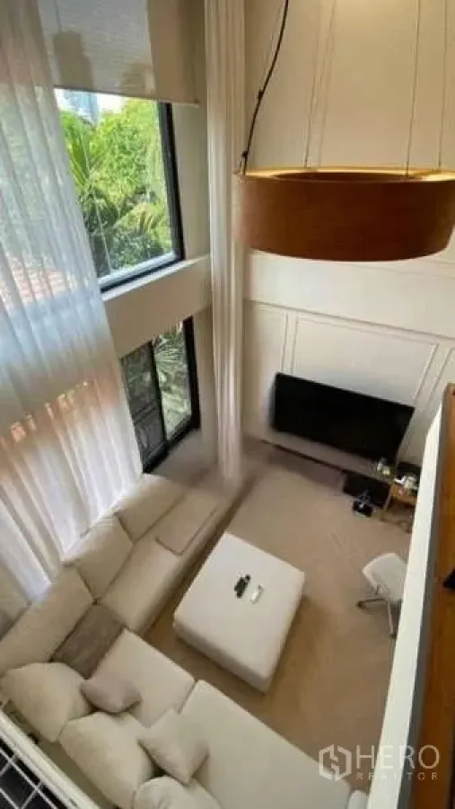Townhouse for rent - Aerial view of a double-height living room with an L-shaped sofa, ottoman, TV, and large pendant light.