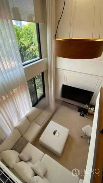 Townhouse for rent - Aerial view of a double-height living room with an L-shaped sofa, ottoman, TV, and large pendant light.