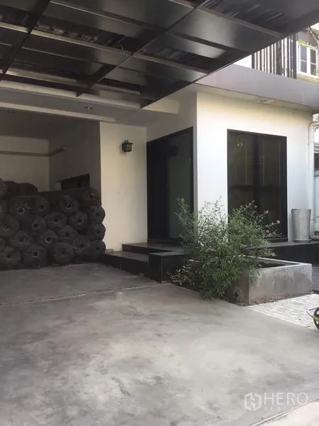 带办公室的家 出租在Suan Luang, Bangkok - 带顶棚的车库与主入口，混凝土地面与绿植点缀。