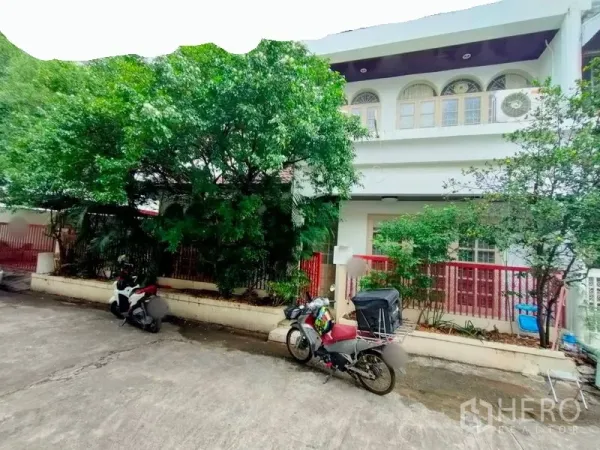 ทาวน์เฮาส์ ให้เช่าในKhlong Toei, Bangkok - ทาวน์เฮ้าส์สองชั้นด้านหน้า มีหน้าต่างโค้ง รั้วสีแดง และต้นไม้ใหญ่ในซอยเงียบสงบ