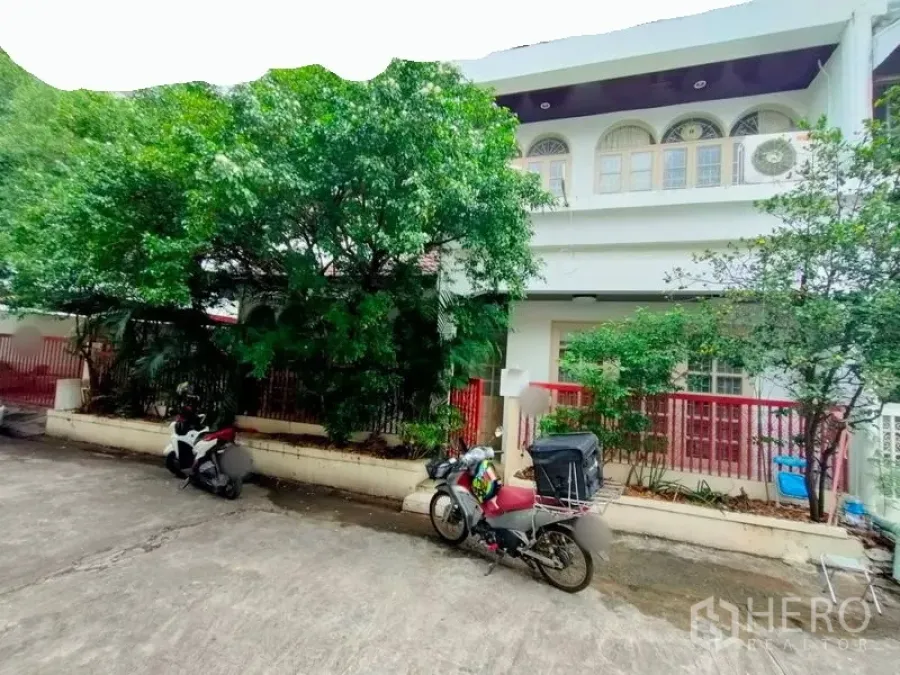 ทาวน์เฮาส์ ให้เช่าในKhlong Toei, Bangkok - ทาวน์เฮ้าส์สองชั้นด้านหน้า มีหน้าต่างโค้ง รั้วสีแดง และต้นไม้ใหญ่ในซอยเงียบสงบ