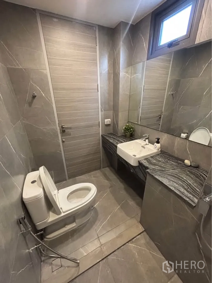 Home Office for rent or sale in Suan Luang, Bangkok - Modern bathroom with gray marble-style tiles, toilet, and wall-mounted sink.