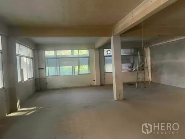 Home Office for rent in Watthana, Bangkok - Spacious empty office level with corner windows, a support column and a ladder in a raw space.