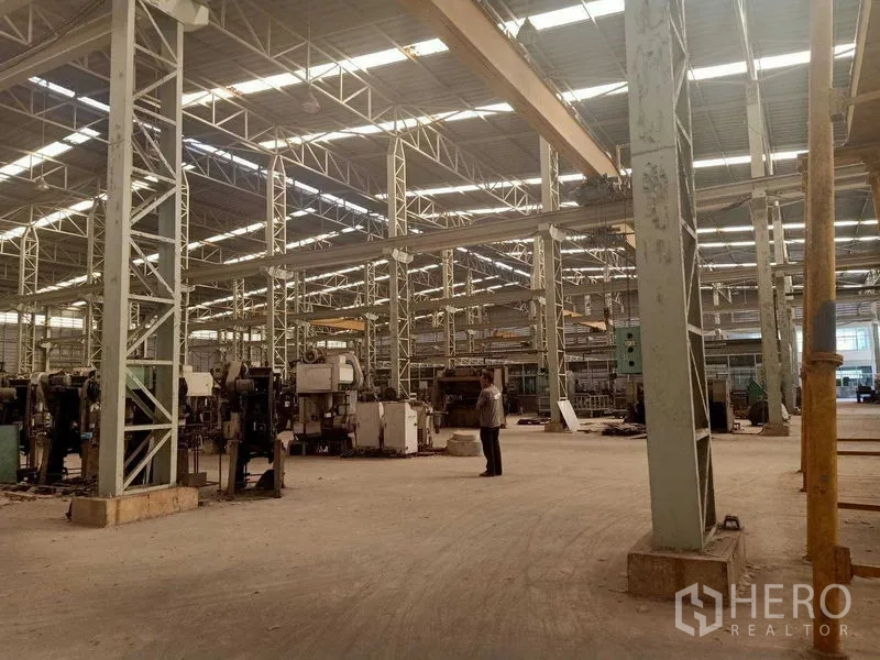 Warehouse for rent in Mueang Samut Sakhon, Samut Sakhon - Wide production bay featuring steel columns, crane beams and heavy equipment on the floor.