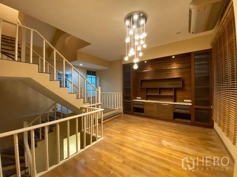 联排别墅 出租在Lat Phrao, Bangkok - 楼上一体家庭厅，内置电视墙、木地板与造型吊灯，毗邻楼梯。