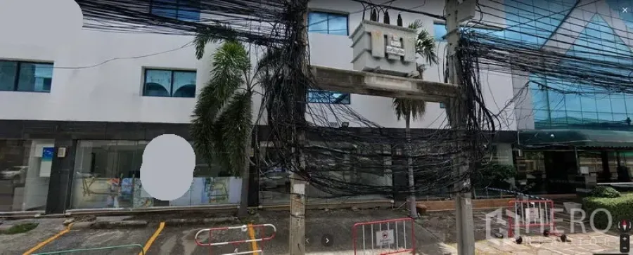 Office Space for rent in Watthana, Bangkok - Modern office building exterior in Watthana, Bangkok with glass facade, palm trees, on-site parking bays and overhead utility cables.